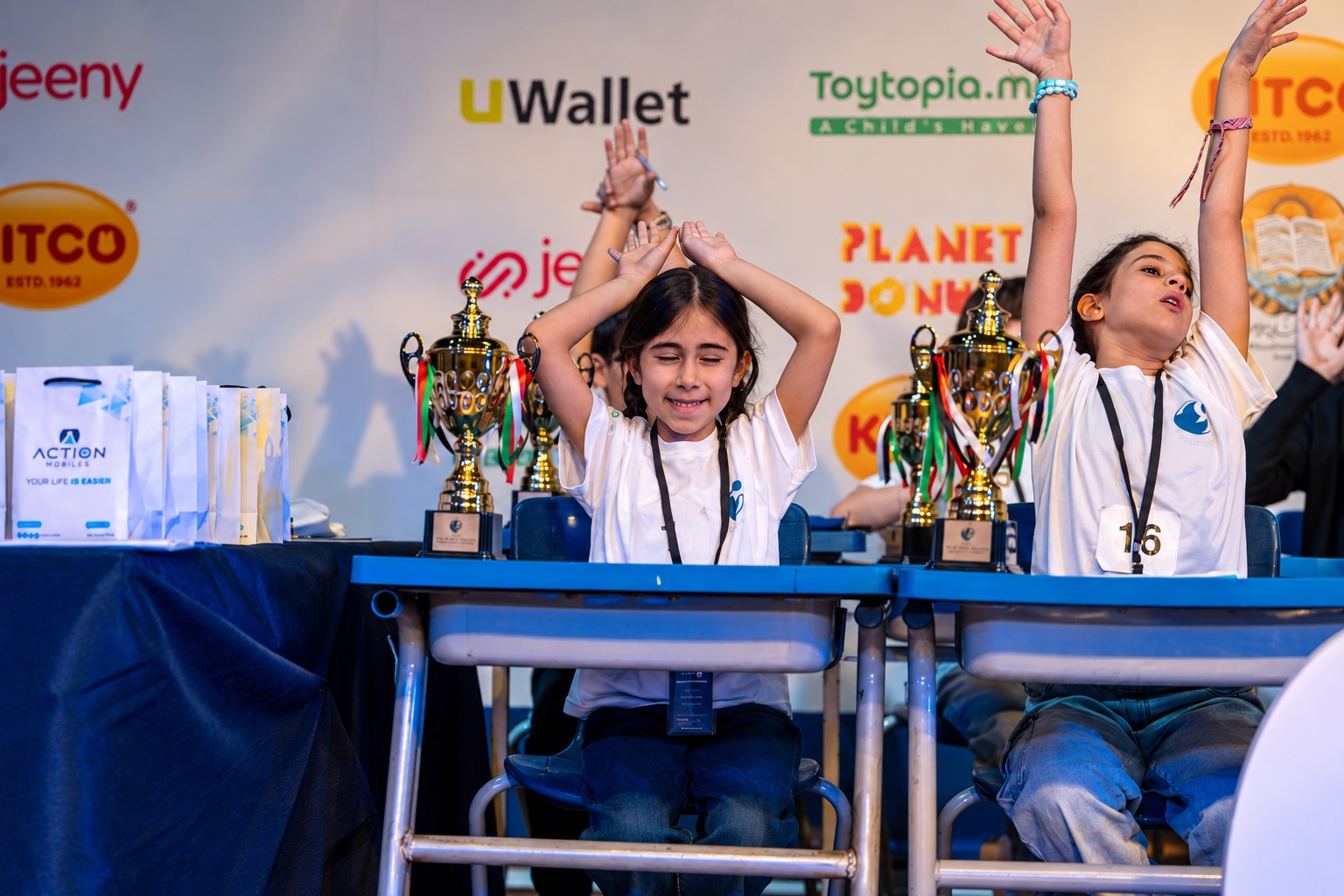 Two Little Genius students celebrating a challenge beside competition trophies